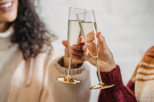 Smiling crop woman with curly hair toasting with champagne while congratulating friend with holiday